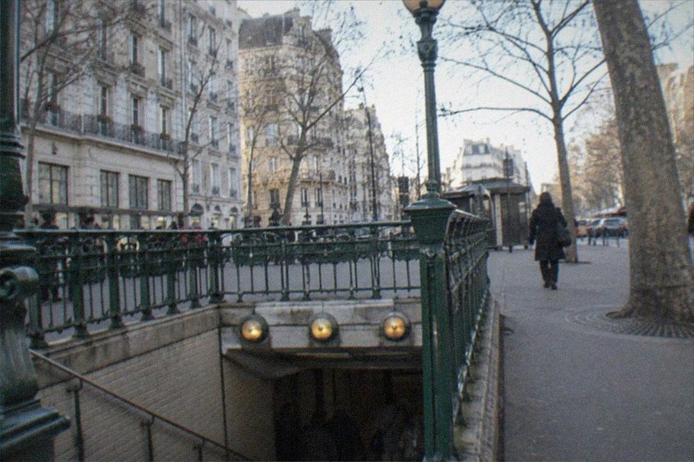 A Metro station entrance with its green railing and lamp sign on a Paris street
