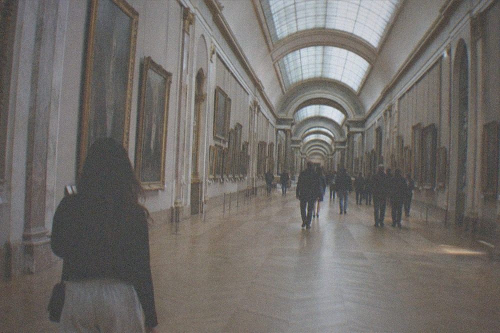 Long picture gallery with paintings in gilded frames along both walls under a glass ceiling