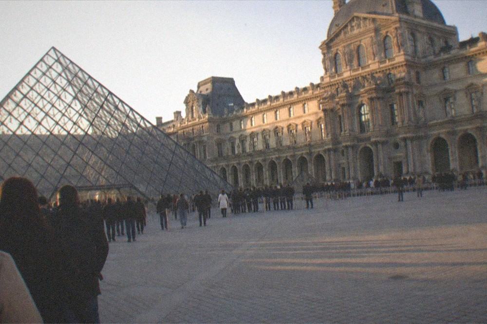 Museum forecourt with glass pyramid and orderly queue barriers at opening time