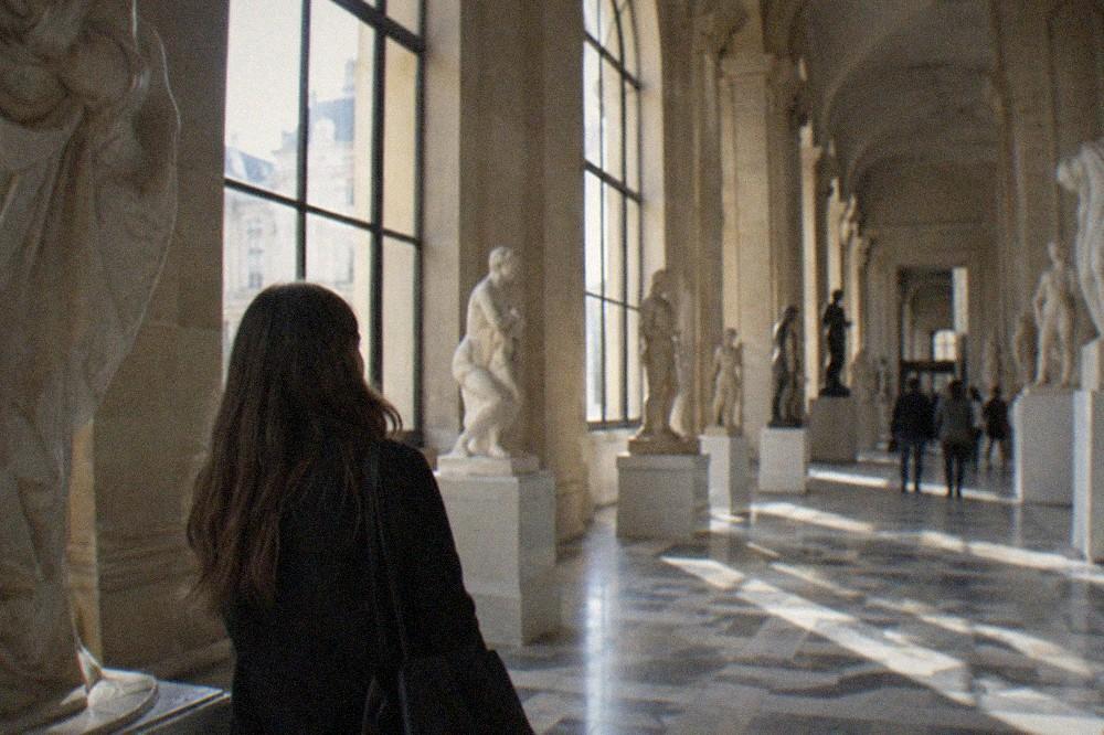 Sunlit museum interior in Paris with a long gallery of sculptures and tall windows