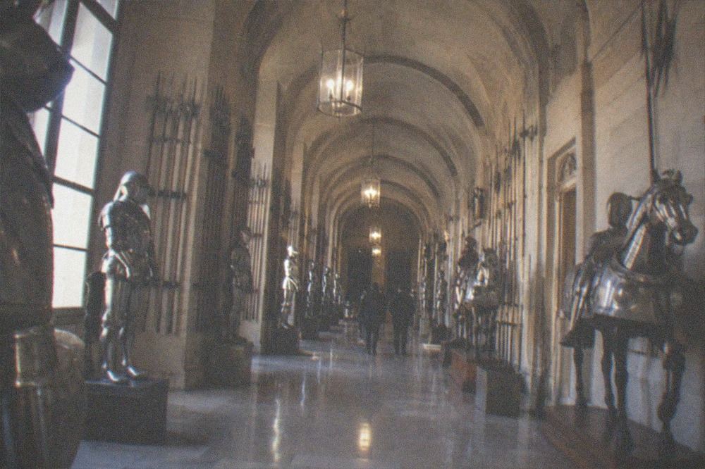 Armory hall with suits of armour and weapons displayed along a stone vaulted gallery