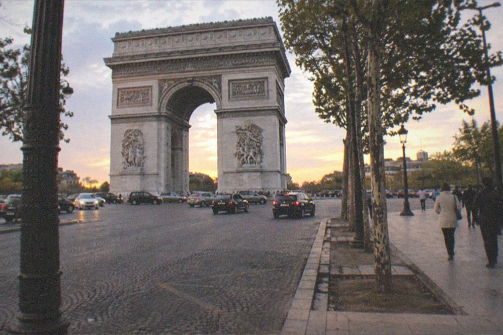 Wide Paris plaza with a landmark arch and light traffic under an evening sky