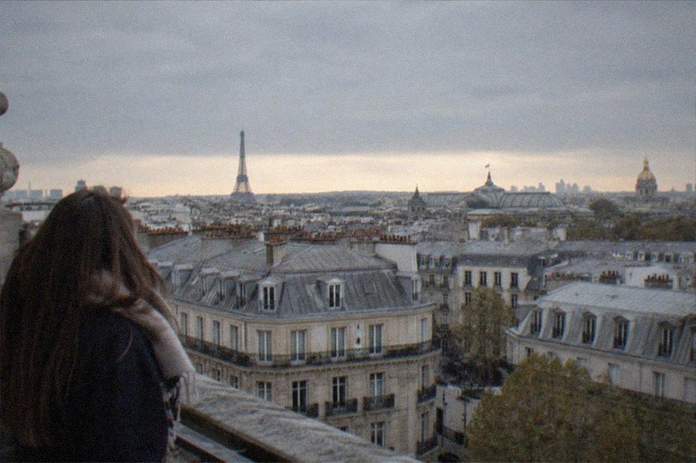 Elevated city view over Paris rooftops toward distant monuments in golden light