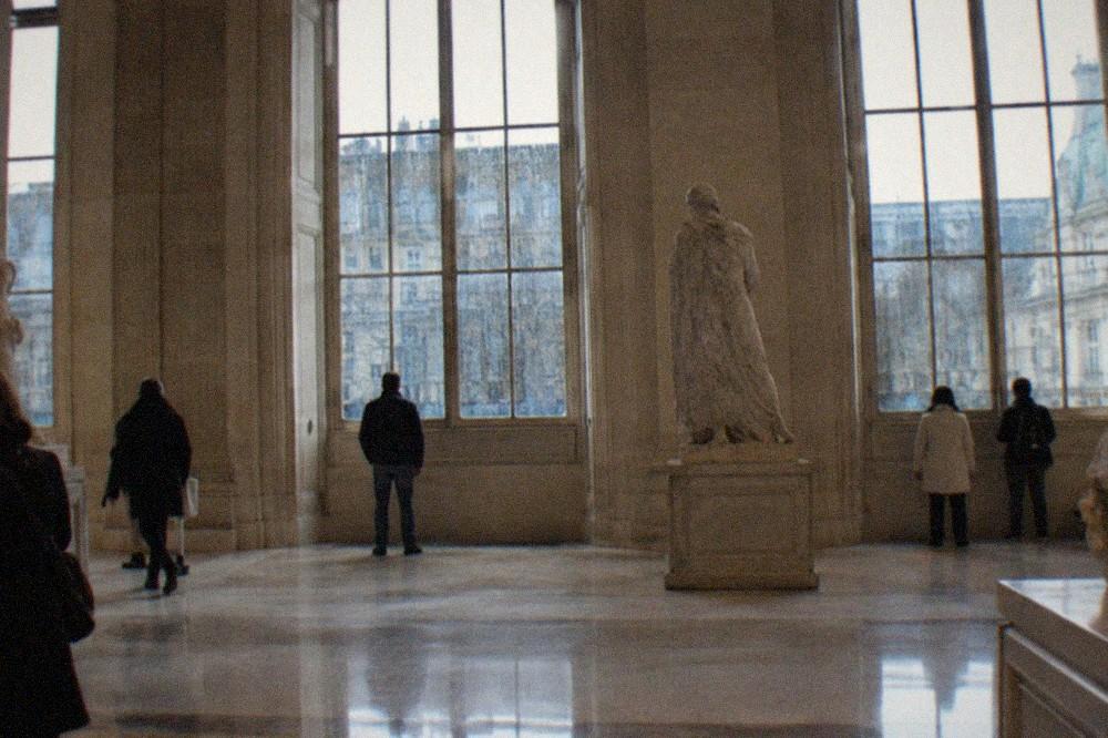 A wide museum gallery with polished stone floors and tall windows streaked with rain