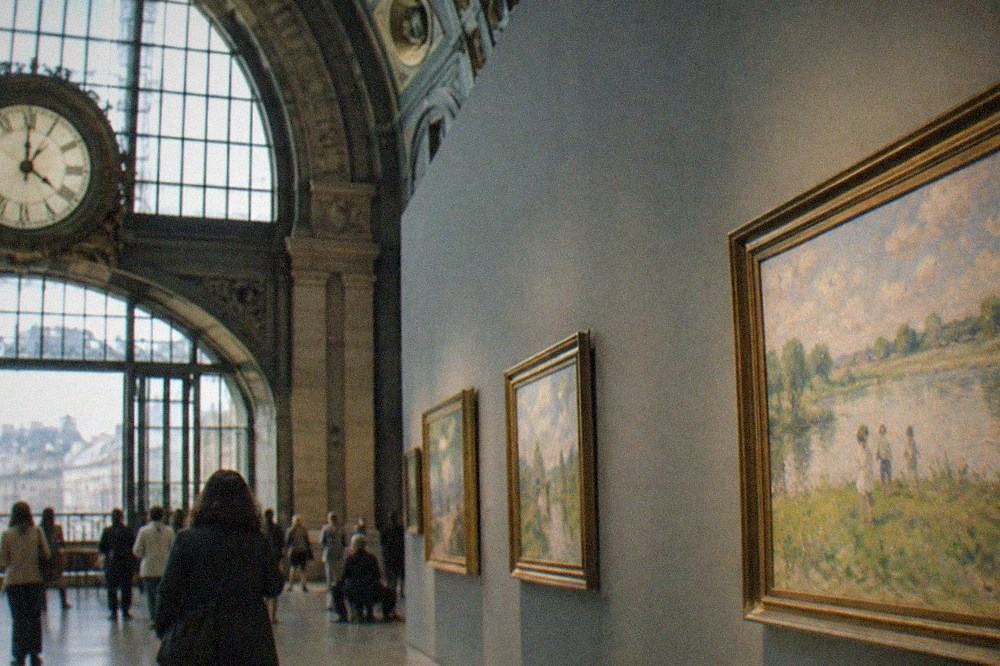 A train station clock above a bright impressionist gallery seen from a dry interior