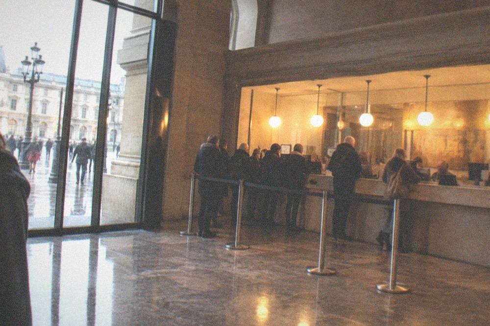 A museum ticket counter under warm lights with rain visible through glass doors