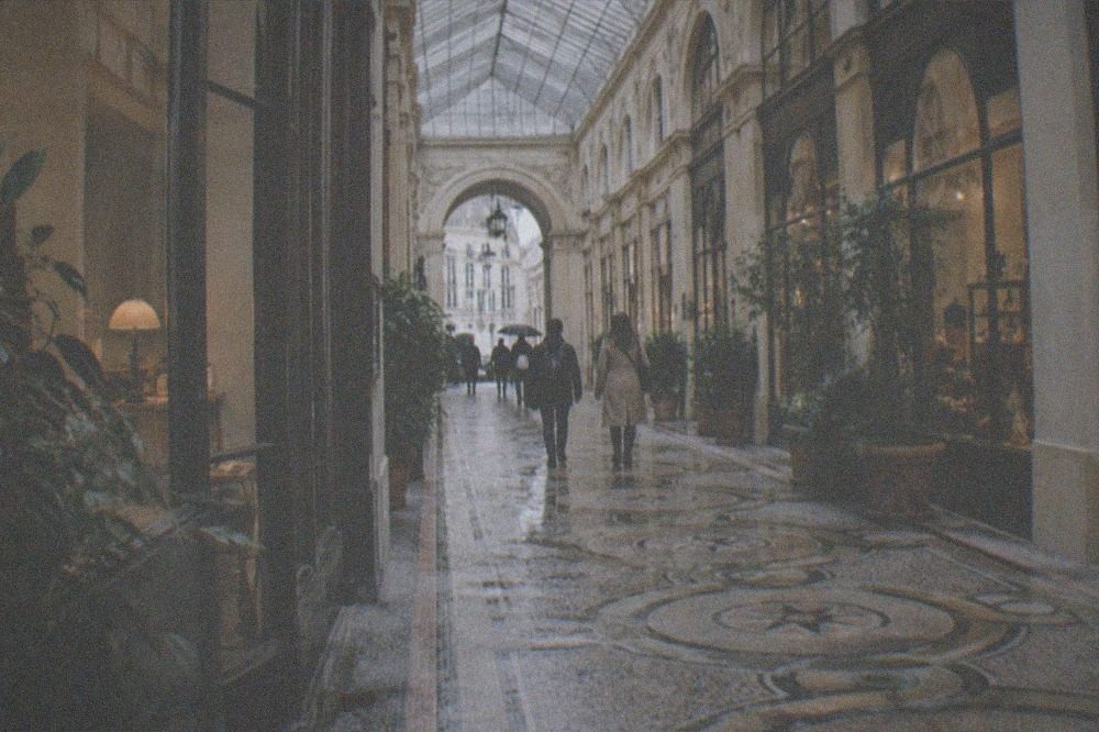 A glass roofed shopping arcade with a mosaic floor lit by daylight