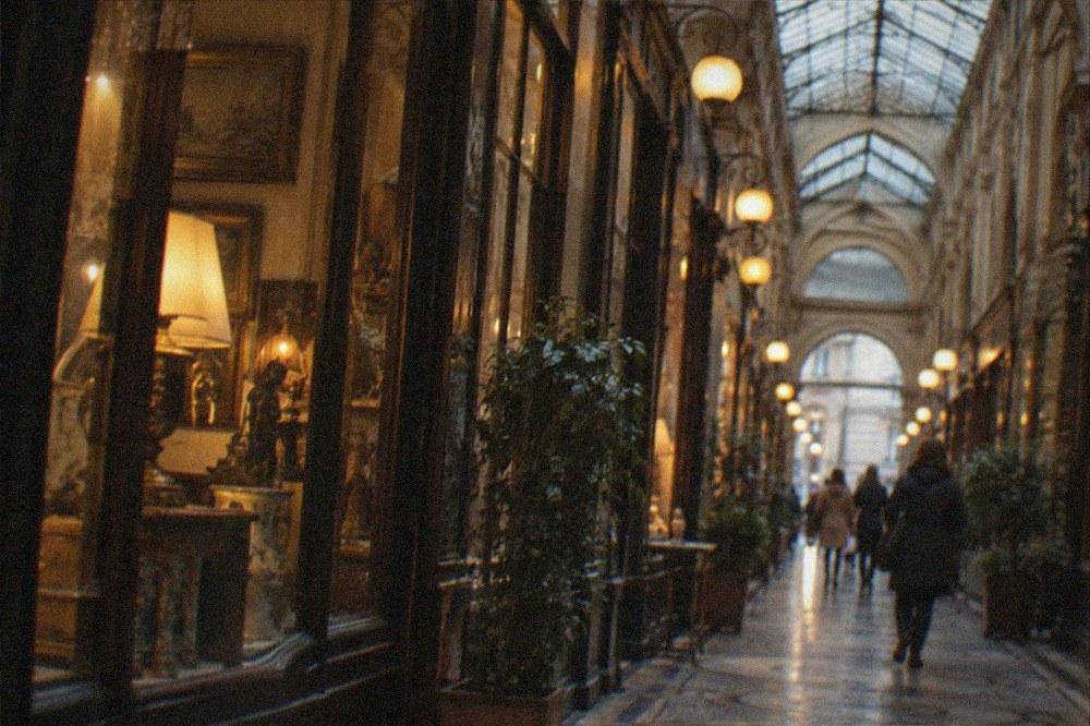 Warm lamplight over a passage arcade with rain streaked glass overhead