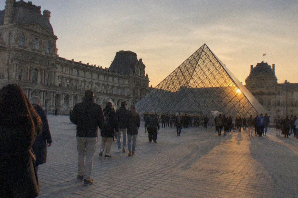 The Louvre pyramid at dusk with visitors crossing the courtyard toward the entrance