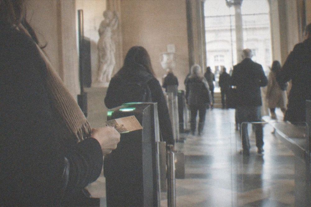A visitor holding a museum pass beside a timed-entry checkpoint inside a Paris museum