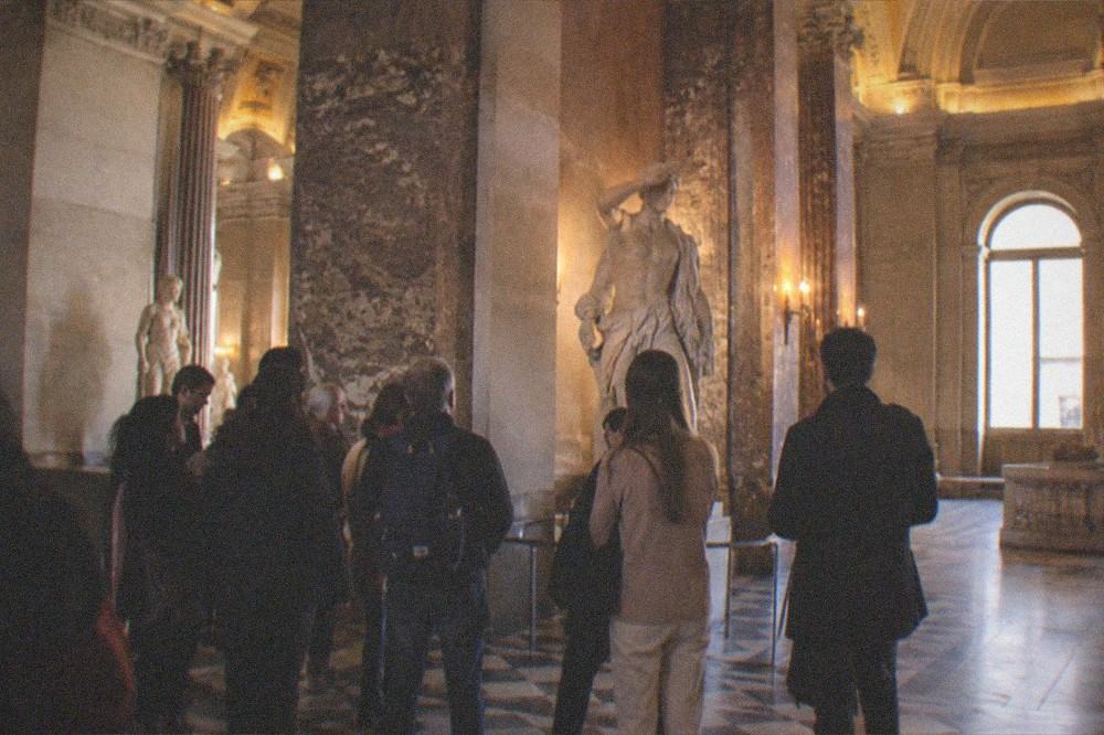 A small tour group gathered around a sculpture in a lit gallery of the Louvre