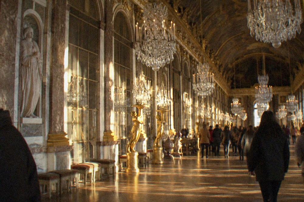 The Hall of Mirrors at Versailles with chandeliers and arched windows reflecting the gallery
