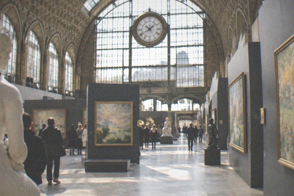 Grand clock-window gallery above a train-shed floor hung with Impressionist canvases
