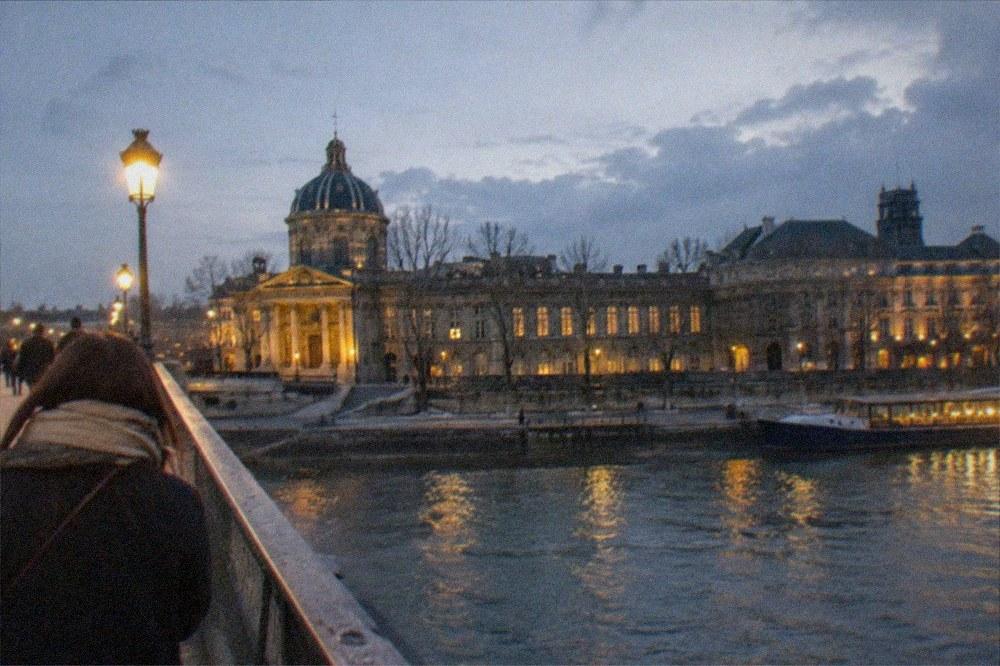 A footbridge over the Seine with museum buildings along the opposite bank in late light