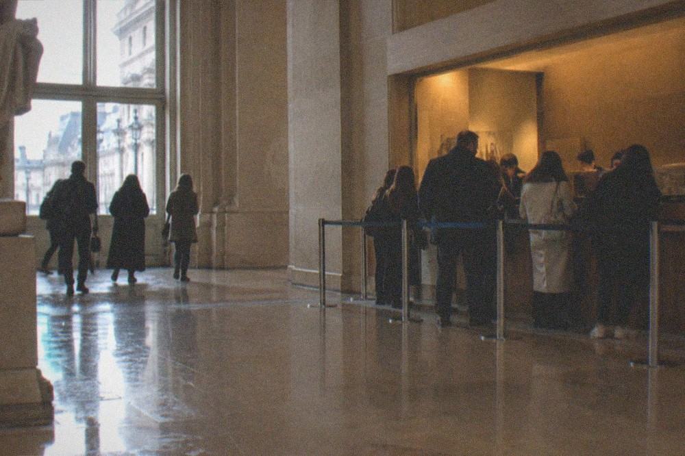 A museum ticket desk with a short orderly queue under warm interior lighting